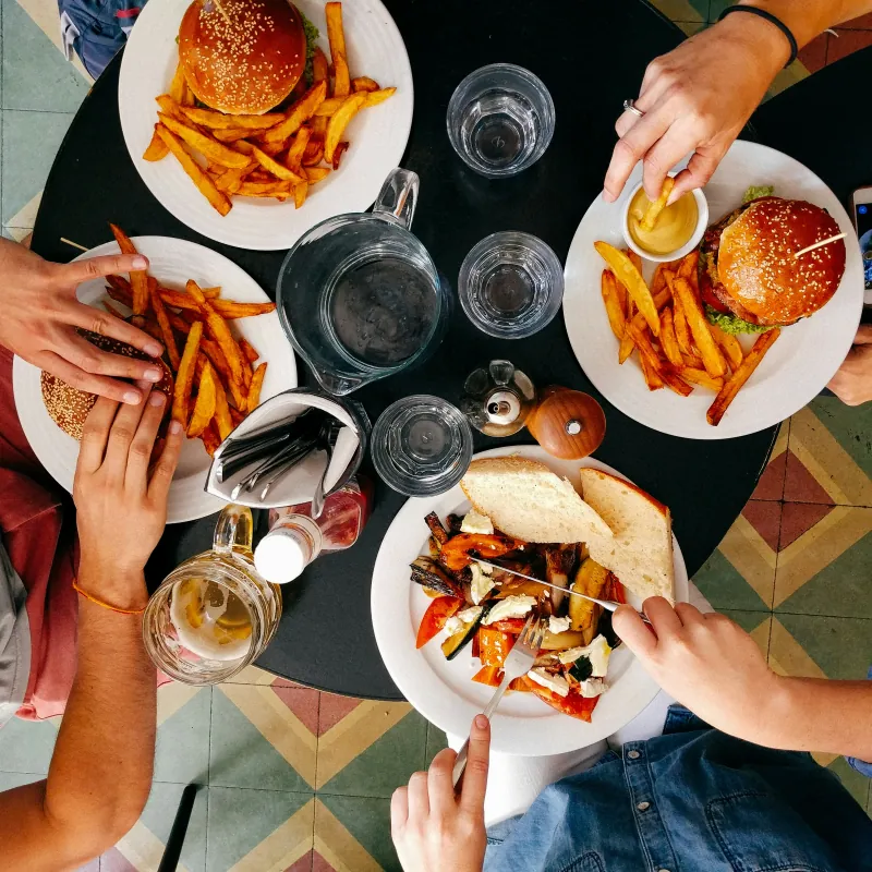 Menschen essen Burger, Pommes und geröstetes Gemüse an einem runden Tisch, von oben gesehen